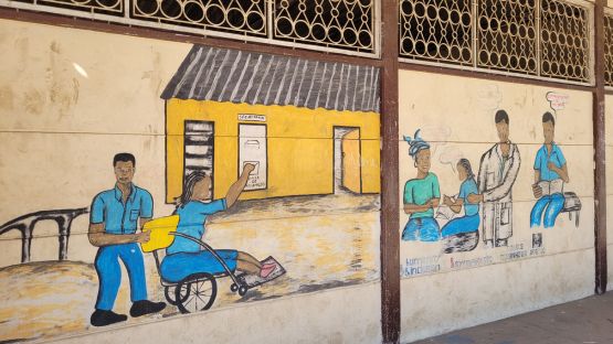 1)	Bild an der Wand der Patrice-Lumumba-Schule in Maputo, das die Begleitung und Betreuung von Kindern mit Behinderungen anhand von Personen illustriert, die das Personal von Handicap International und die Begünstigten darstellen.