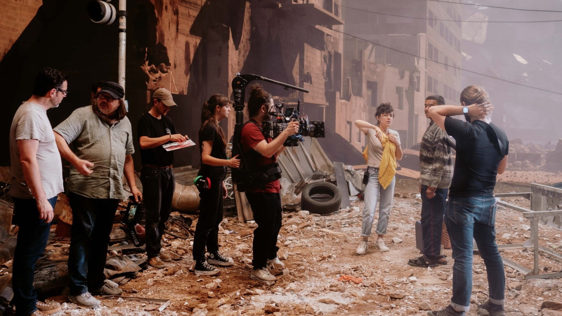 Image du plateau de tournage de la campagne, avec un caméraman et des acteurs dans une ville entièrement détruite 