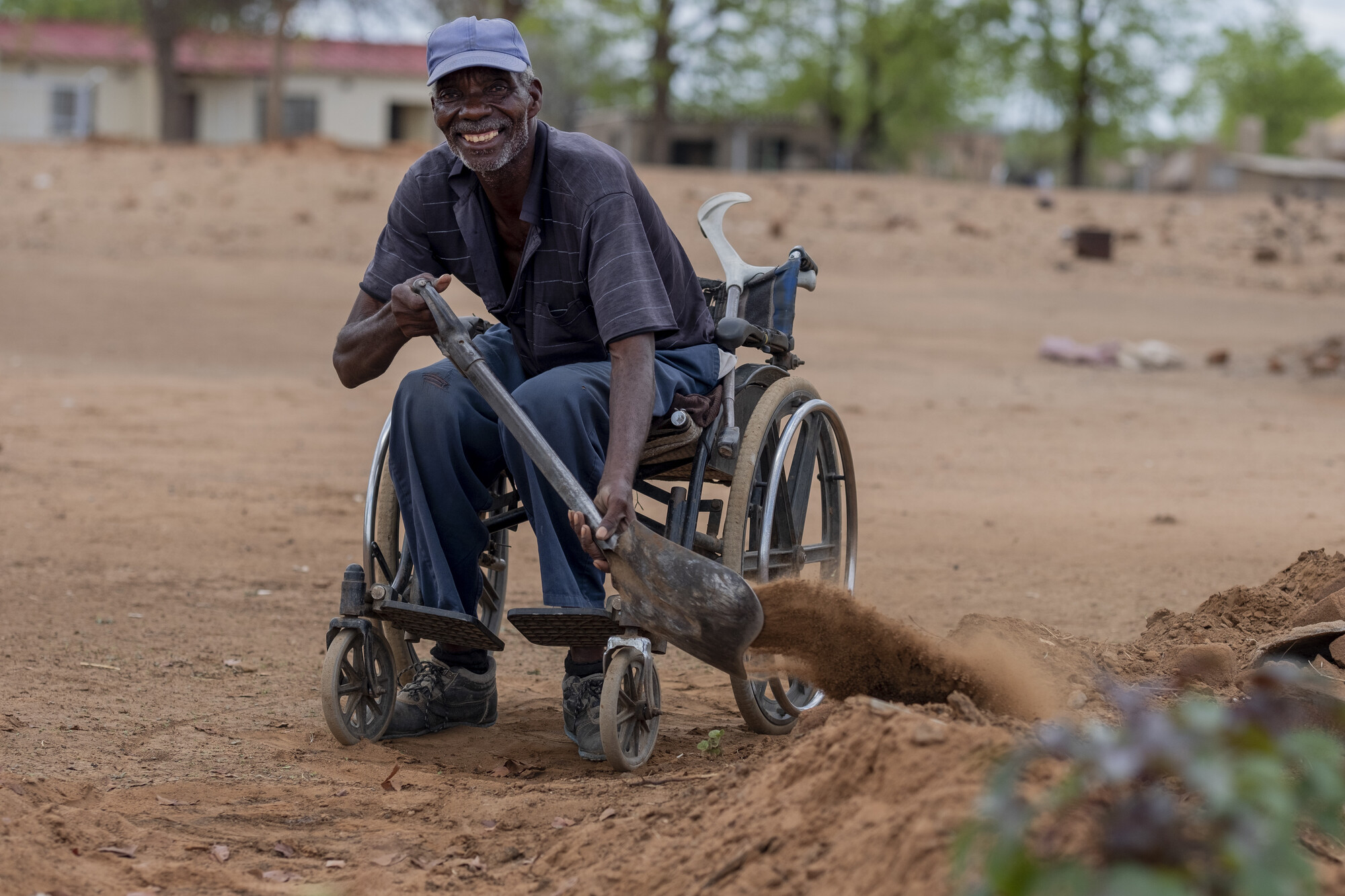 Un monsieur en chaise roulante qui ramasse de la terre à l'aide d'une pelle