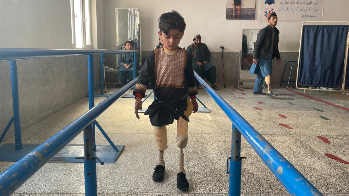 Kleiner Junge, Imran, in der Mitte des Bildes, der mit seinen neuen Prothesen in einem HI-Rehabilitationszentrum in Kandahar laufen lernt. 