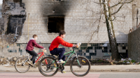 Des garçons passent à vélo devant des bâtiments détruits par la violence armée.