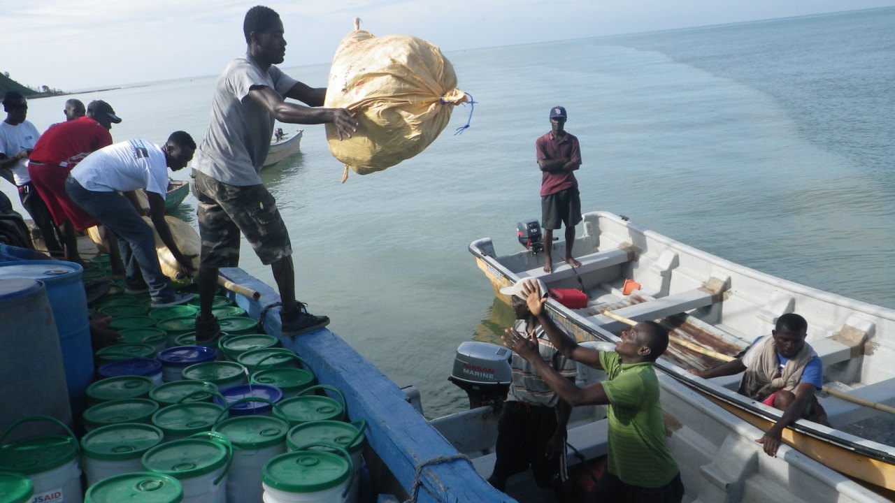 Lokale Mitarbeitende verladen die Säcke und Tonnen der humanitären Güter in kleinere Boote