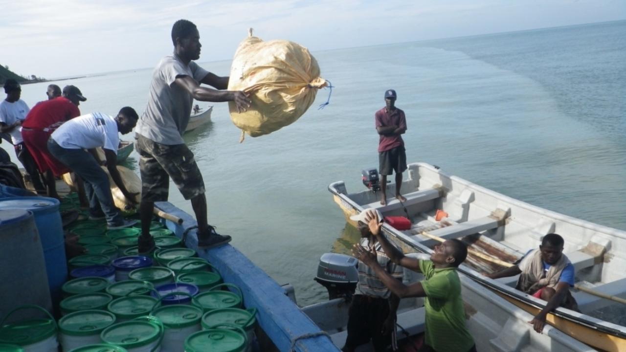 Männer verladen Säcke und Eimer mit Hilfsgütern in die Boote, die die Güter in schwer erreichbare Gegenden bringen werden