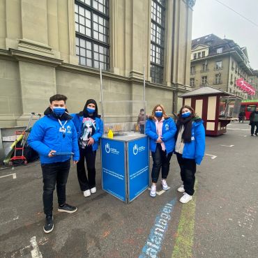 Vier Personen mit blauen Handicap International Jacken um einen Handicap International Stand herum