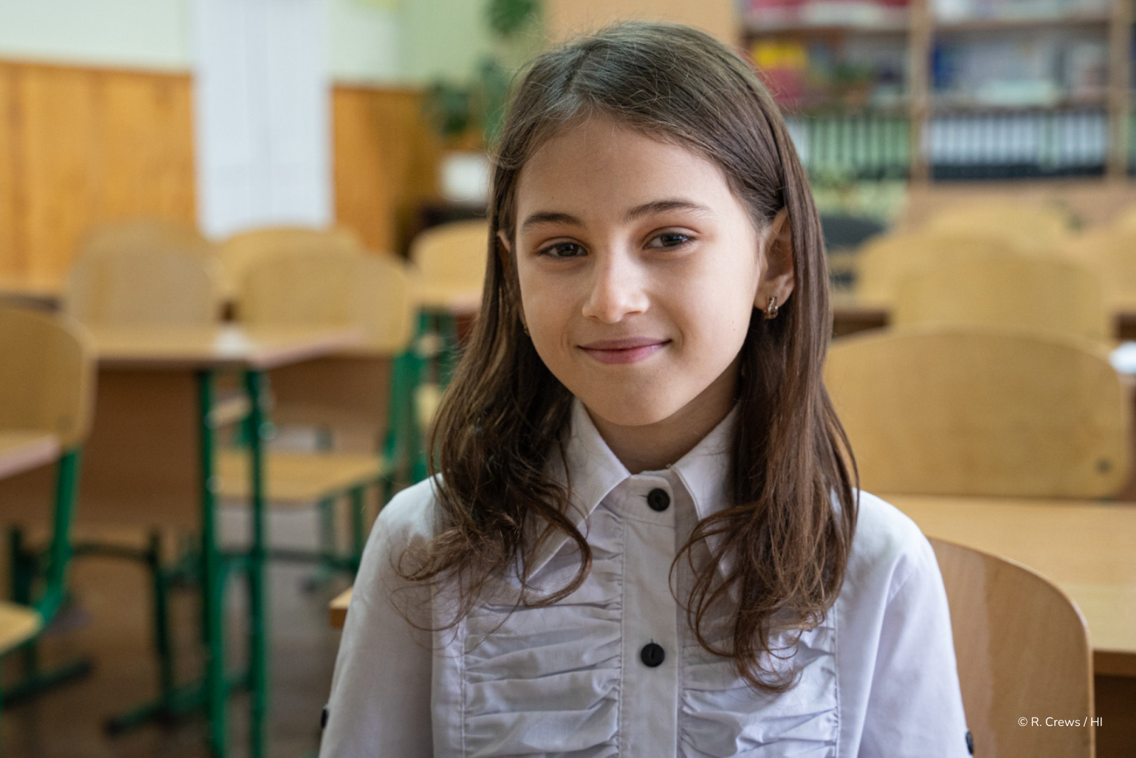 Myroslava, 10 ans, petite fille brune souriant à l’objectif dans une salle de classe à Chernivtsi, participant à une session EORE de sensibilisation aux risques liés aux mines et munitions, organisée par Handicap International.