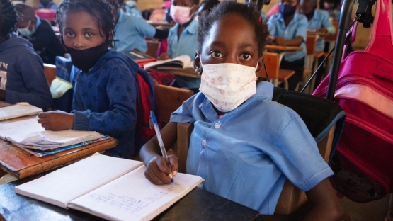 Shelcia, bénéficiaire de Handicap International, assise en classe avec ses camarades. Elle écrit sur un cahier. 