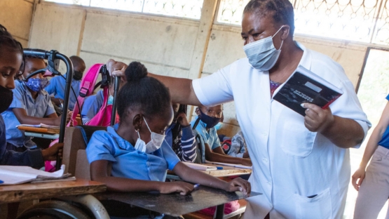 Shelcia, bénéficiaire de HI, dans sa classe et sa professeure Filomena qui tient un livre. 