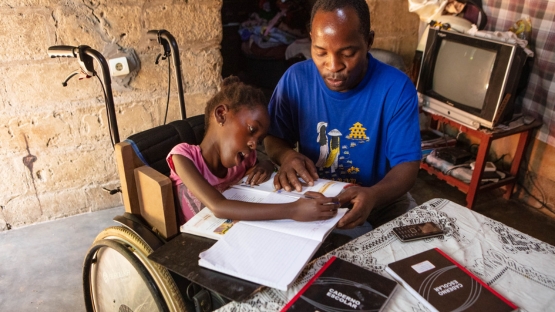 Shelcia est assise à table et fait ses devoirs aux côtés de son père qui l'aide. 