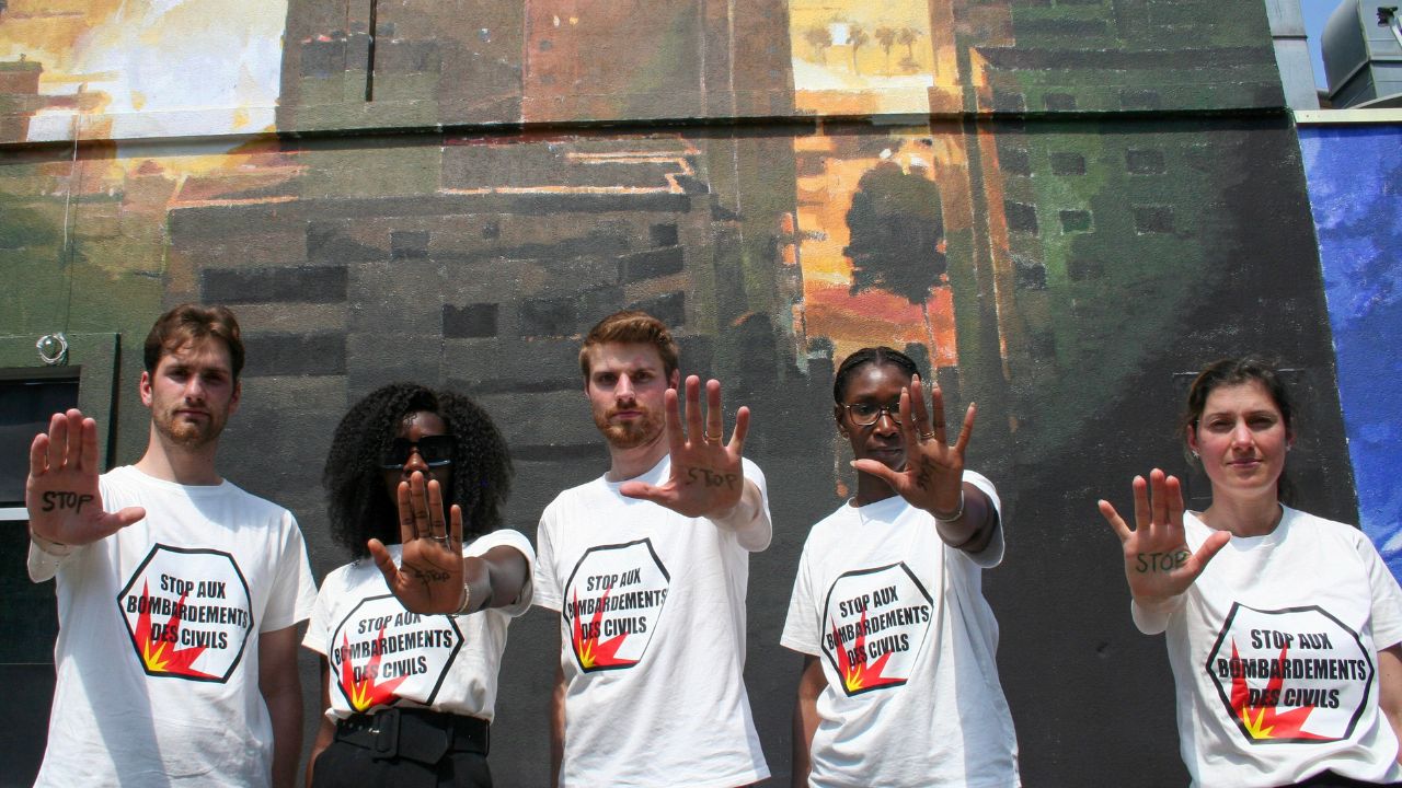 5 personnes sont devant un mur peint et ils portent un t-shirt où il est écrit "Stop Bombing Civilians"