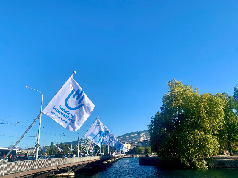 Brücke in Genf mit weißen und blauen Handicap Interntational-Flaggen. Einige sind mit dem Logo beflockt, andere mit Broken Chair