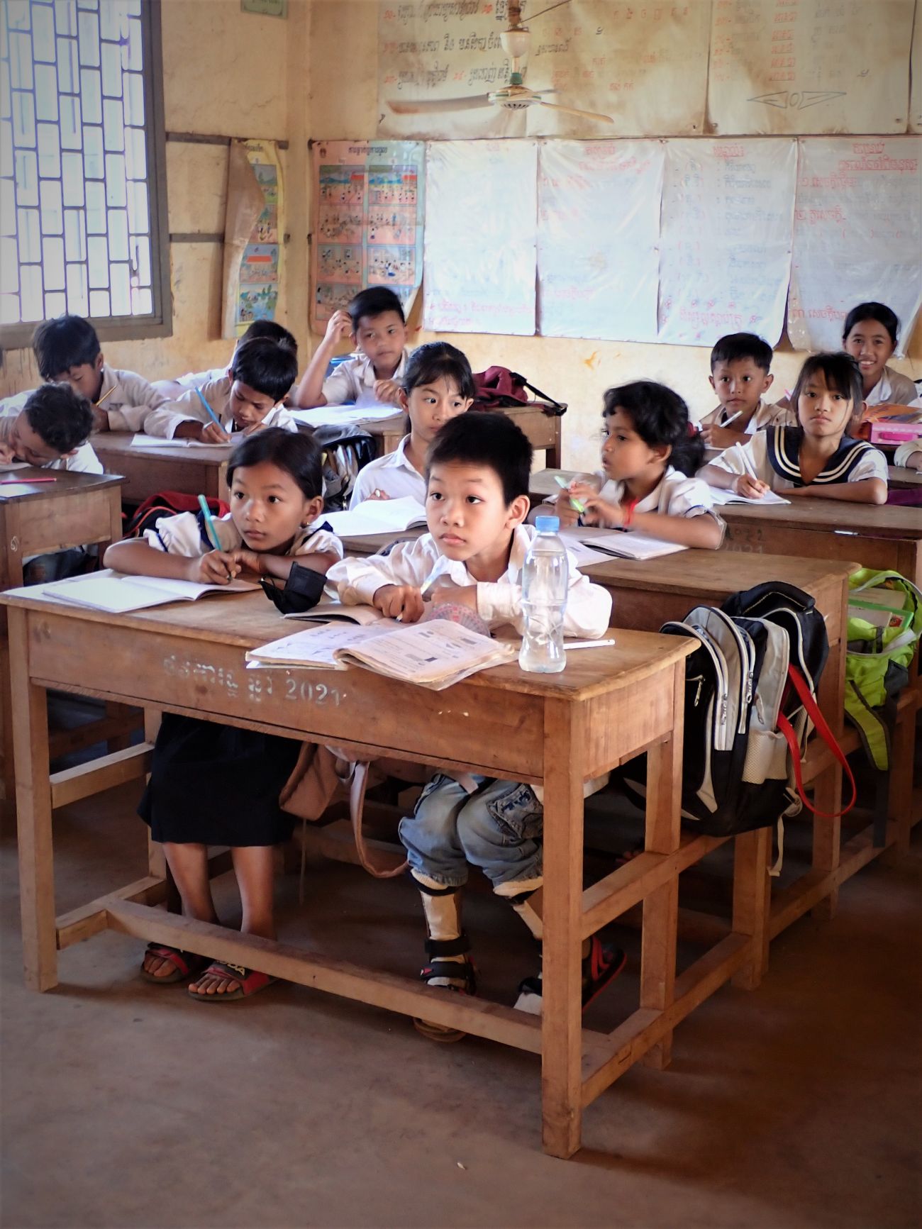 Khim Chanreaksa peut se rendre en classe grâce aux orthèses fournies par HI. Il est au premier rang en train d'écrire sur son cahier