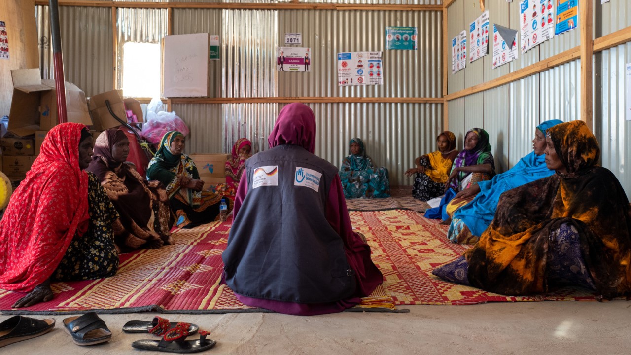 Des femmes sont assises en cercle dans une grande salle, elles discutent en elles, accompagnées par un professionnel de santé mentale.