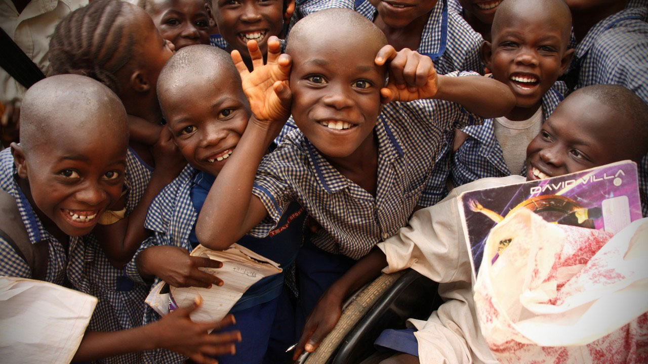 Eine Nahaufnahme einer Gruppe spielender Kinder in Sierra Leone. Sie tragen blau-weiß karierte Schuluniformen.