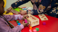 Une enfant qui joue avec des puzzle avec des formes de couleur dans une caisse en bois 