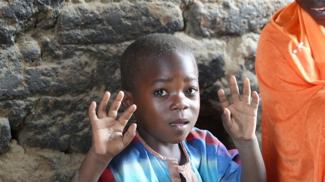 Yacouba regarde la caméra et lève ses deux mains en l'air, paumes ouvertes et doigts tendus.