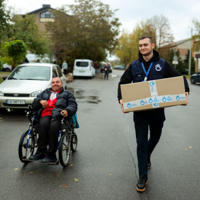 Distribution de kits d'hygiène par un membre HI avec à côté de lui un bénéficiaire en fauteuil roulant